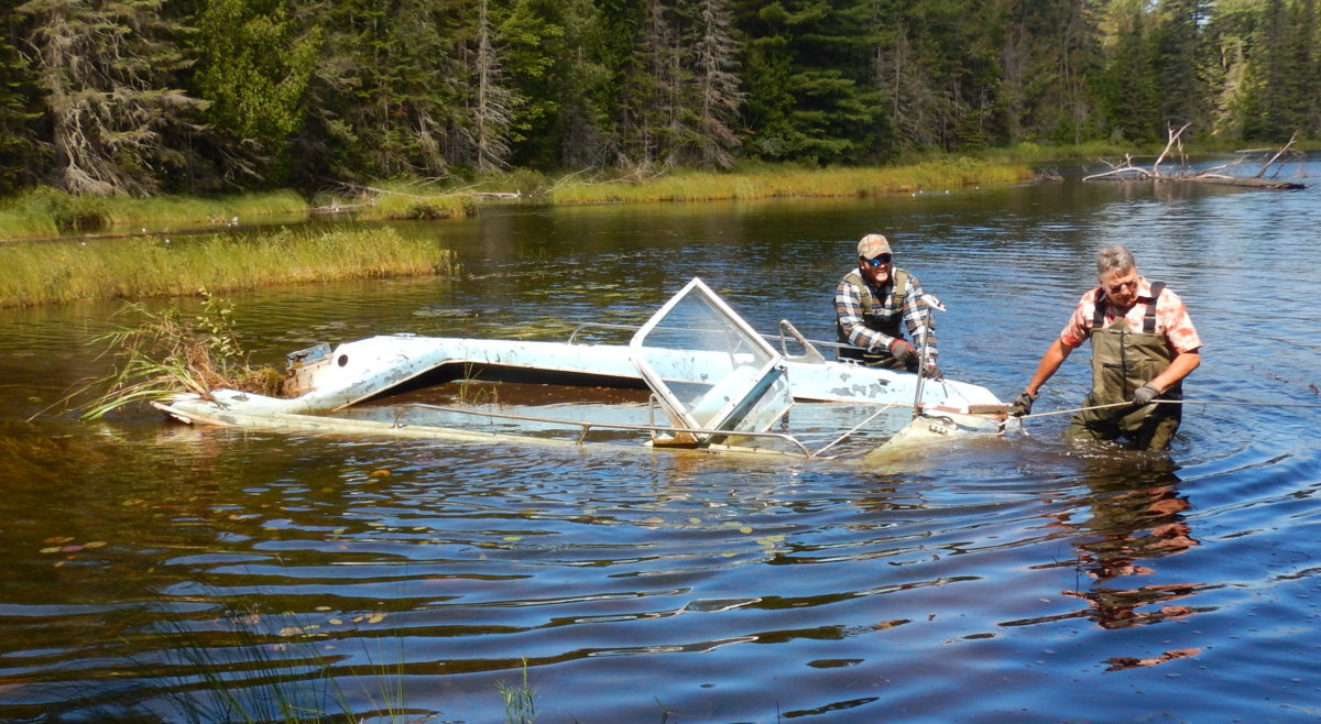 photo of two men pulling a waterlogged boat in the water